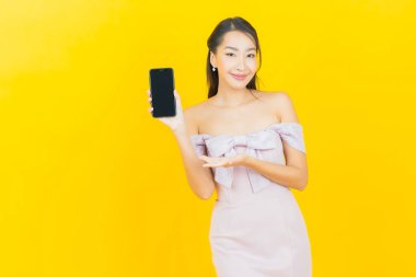 Renkli arka planda akıllı cep telefonuyla güzel Asyalı kadın gülümsemesi