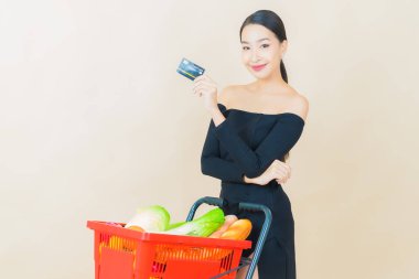 Renkli arka planda süpermarketten alınmış market sepetiyle gülümseyen güzel Asyalı kadın portresi.