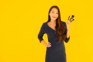 Sarı izole arkaplanda makyaj fırçası olan güzel bir Asyalı kadın portresi.