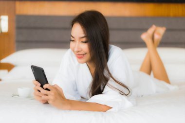 Güzel bir Asyalı kadın yatak odasının içinde akıllı cep telefonu kullanıyor.