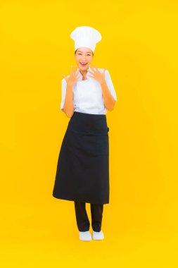 Güzel bir Asyalı kadın portresi ya da sarı izole arkaplanda şapkası olan aşçı üniforması.