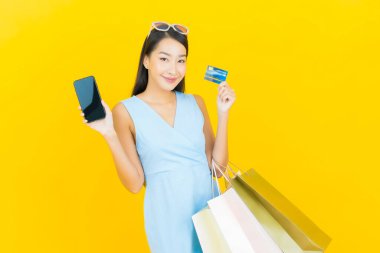 Sarı arka planda alışveriş çantasıyla gülümseyen güzel Asyalı kadın portresi