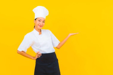Güzel bir Asyalı kadın portresi ya da sarı izole arkaplanda şapkası olan aşçı üniforması.