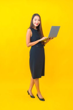 Sarı arka planda dizüstü bilgisayarı olan güzel Asyalı iş kadını portresi