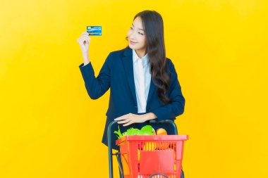 Renkli arka planda süpermarketten alınmış market sepetiyle gülümseyen güzel Asyalı kadın portresi.