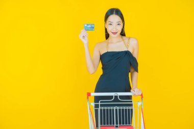 Renkli arka planda süpermarketten alınmış market sepetiyle gülümseyen güzel Asyalı kadın portresi.