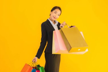 Sarı izole edilmiş arka planda alışveriş merkezinden alışveriş çantasıyla güzel bir genç Asyalı kadın portresi.