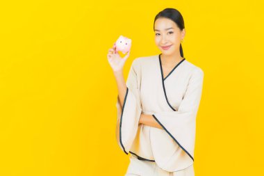 Bir sürü parası ve sarı arka planda kumbarası olan Asyalı güzel bir iş kadını portresi.