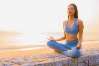Genç Asyalı kadının portresi sağlık için gün doğumunda deniz kıyısı okyanusunda meditasyon yapıyor.