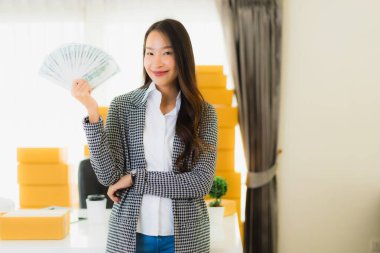 Güzel Asyalı bir kadının portresi dizüstü bilgisayarından nakit para ve karton kutuyla çevrimiçi müşteri alışverişi için hazır.