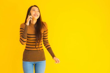 Güzel genç Asyalı kadın, sarı izole edilmiş arka planda birçok eylem içeren akıllı cep telefonu ya da cep telefonu kullanır.