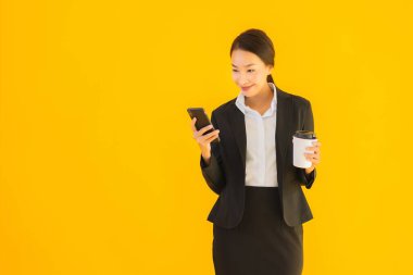 Portre güzel genç Asyalı kadın akıllı cep telefonu ve kahve fincanı ile izole edilmiş sarı arka planda