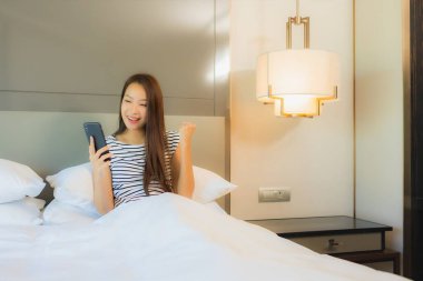 Güzel bir Asyalı kadın yatak odasının içinde akıllı cep telefonu kullanıyor.