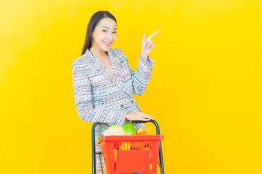 Renkli arka planda süpermarketten alınmış market sepetiyle gülümseyen güzel Asyalı kadın portresi.