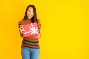 Güzel bir Asyalı kadın portresi. Mutlu bir gülümseme. Sarı izole edilmiş arka planda kırmızı hediye kutusu var.