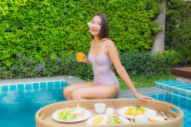 Genç Asyalı kadının portresi mutlu bir gülümseme ile otel havuzunda yüzen kahvaltı tepsisinin keyfini çıkar.