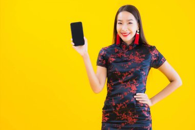 Güzel bir portre genç Asyalı kadın Çin elbisesi giyer Çin 'in yeni yıl konsepti için sarı izole edilmiş arka planda akıllı cep telefonu kullanır.