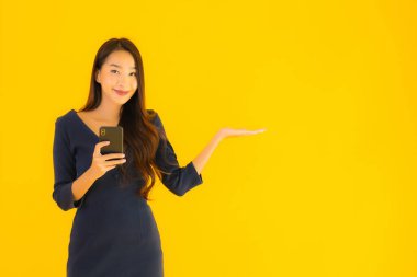 Akıllı cep telefonlu güzel Asyalı kadın portresi ya da sarı izole edilmiş arka planda cep telefonu.