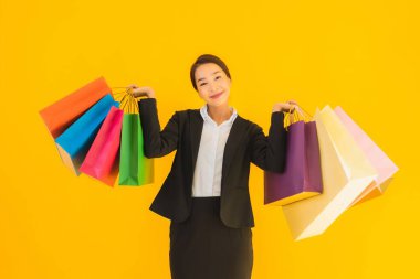 Sarı izole edilmiş arka planda alışveriş merkezinden alışveriş çantasıyla güzel bir genç Asyalı kadın portresi.