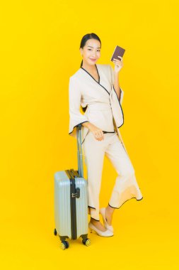 Güzel, genç, iş kadını, bavul ve pasaportlu Asyalı kadın, sarı arka planda seyahat etmeye hazır.