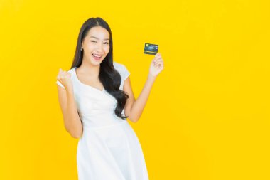Asyalı güzel bir kadının portresi. Sarı arka planda kredi kartıyla gülümsüyor.