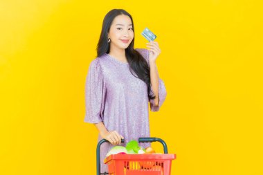 Renkli arka planda süpermarketten alınmış market sepetiyle gülümseyen güzel Asyalı kadın portresi.