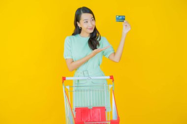 Renkli arka planda süpermarketten alınmış market sepetiyle gülümseyen güzel Asyalı kadın portresi.