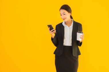 Portre güzel genç Asyalı kadın akıllı cep telefonu ve kahve fincanı ile izole edilmiş sarı arka planda