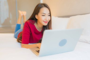 Güzel bir Asyalı kadın yatak odasının içinde dizüstü bilgisayar kullanıyor.