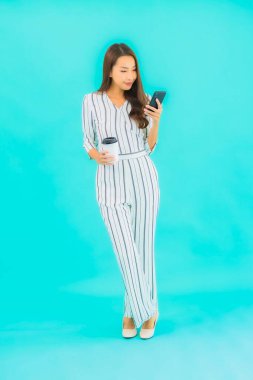 Güzel bir Asyalı kadın portresi mavi arka planda akıllı cep telefonu kullanıyor.