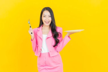 Asyalı güzel bir kadının portresi. Sarı arka planda boş tabak tabağıyla gülümsüyor.