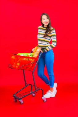 Marketten aldığı alışveriş sepetiyle kırmızı izole arka planda güzel bir Asyalı kadın portresi.