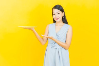 Güzel Asyalı bir kadının portresi. Arka planda boş tabak tabağıyla gülümsüyor.