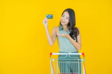 Renkli arka planda süpermarketten alınmış market sepetiyle gülümseyen güzel Asyalı kadın portresi.