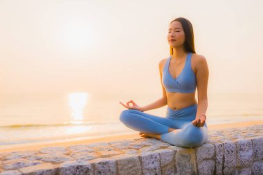 Genç Asyalı kadının portresi sağlık için gün doğumunda deniz kıyısı okyanusunda meditasyon yapıyor.