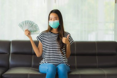 Maskeli güzel Asyalı kadının portresi evde para ya da para gösteriyor.