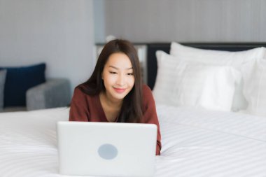 Güzel bir Asyalı kadın yatak odasının iç kısmında bilgisayar kullanıyor.