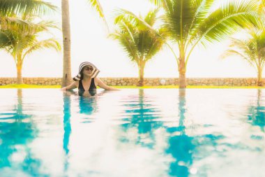 Güzel bir Asyalı kadın portresi, gün batımında palmiye ağacıyla birlikte havuz kenarında dinleniyor ya da tatil için gün doğumunda dinleniyor.