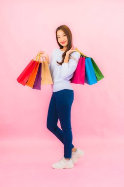 Portrait beautiful young asian woman with colorful shopping bag on pink color isolated background