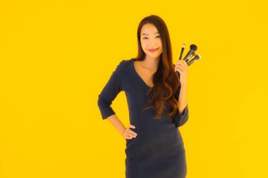 Sarı izole arkaplanda makyaj fırçası olan güzel bir Asyalı kadın portresi.