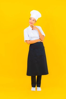 Güzel bir Asyalı kadın portresi ya da sarı izole arkaplanda şapkası olan aşçı üniforması.
