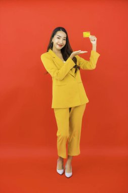 Güzel bir Asyalı kadının portresi kırmızı arka planda kredi kartıyla cep telefonu kullanıyor.