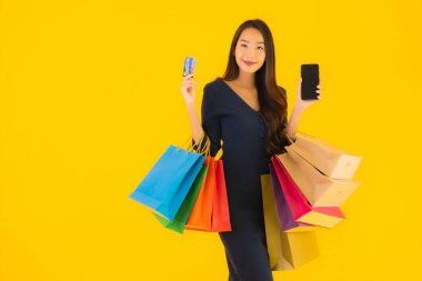 Portre güzel genç Asyalı kadın alışveriş çantası kredi kartı ve akıllı cep telefonu sarısı izole bir arka plan.