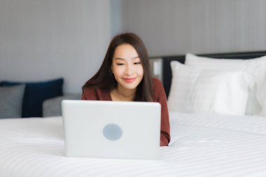 Güzel bir Asyalı kadın yatak odasının iç kısmında bilgisayar kullanıyor.