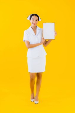 Güzel bir Asyalı genç kadın portresi boş beyaz pano gösteriyor ve sarı izole edilmiş arka planda klinik ya da hastanede çalışıyor.