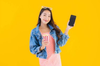 Güzel bir Asyalı kadın portresi telefon patlamış mısırı ve sarı izole edilmiş bir arka planda film izlemekten memnun.