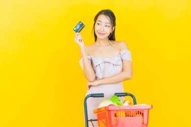 Renkli arka planda süpermarketten alınmış market sepetiyle gülümseyen güzel Asyalı kadın portresi.