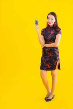 Portrait beautiful young asian woman wear chinese dress with credit card and smart mobile phone on yellow isolated background clipart