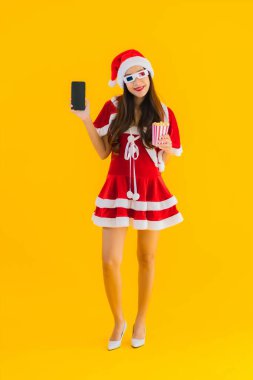 Güzel bir Asyalı kadın portresi patlamış mısır ve 3D gözlüklü noel şapkası takıyor sarı izole edilmiş arka planda film izlemeye hazır.