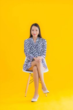 Güzel bir Asyalı kadın, sarı izole edilmiş arka planda hareketli bir şekilde sandalyede oturuyor.